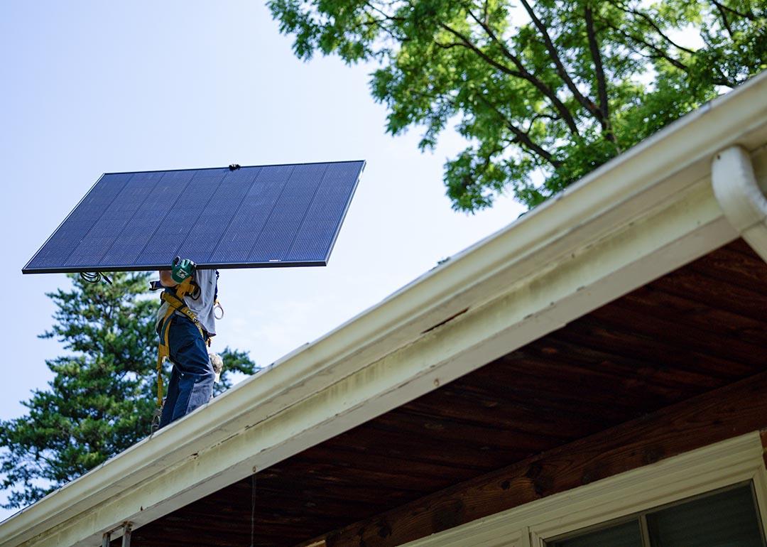 Michael Reimann, installer with Lumina Solar, carries a large panel and his face is not visible while installs solar panels on the roof of a home in Kensington, MD on July 3, 2025.