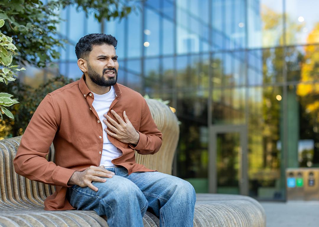 A young man nervously sitting on a bench outdoors experiencing chest pains.