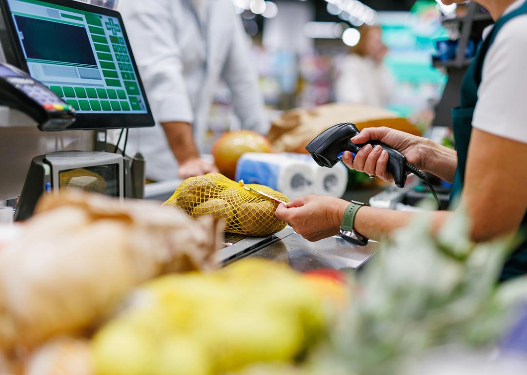 A supermarket cashier staff scans a bag of potatoes at a checkout counter.
