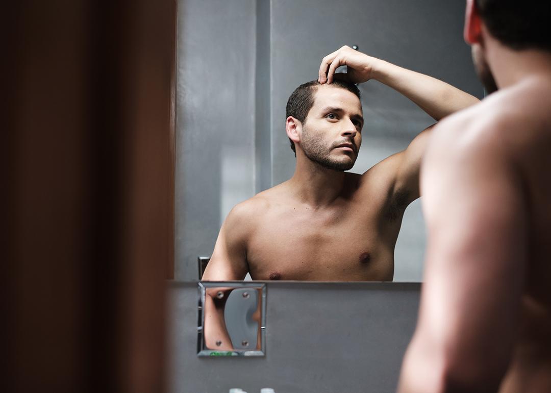 A man looks himself at the mirror inspecting his receding hairline.