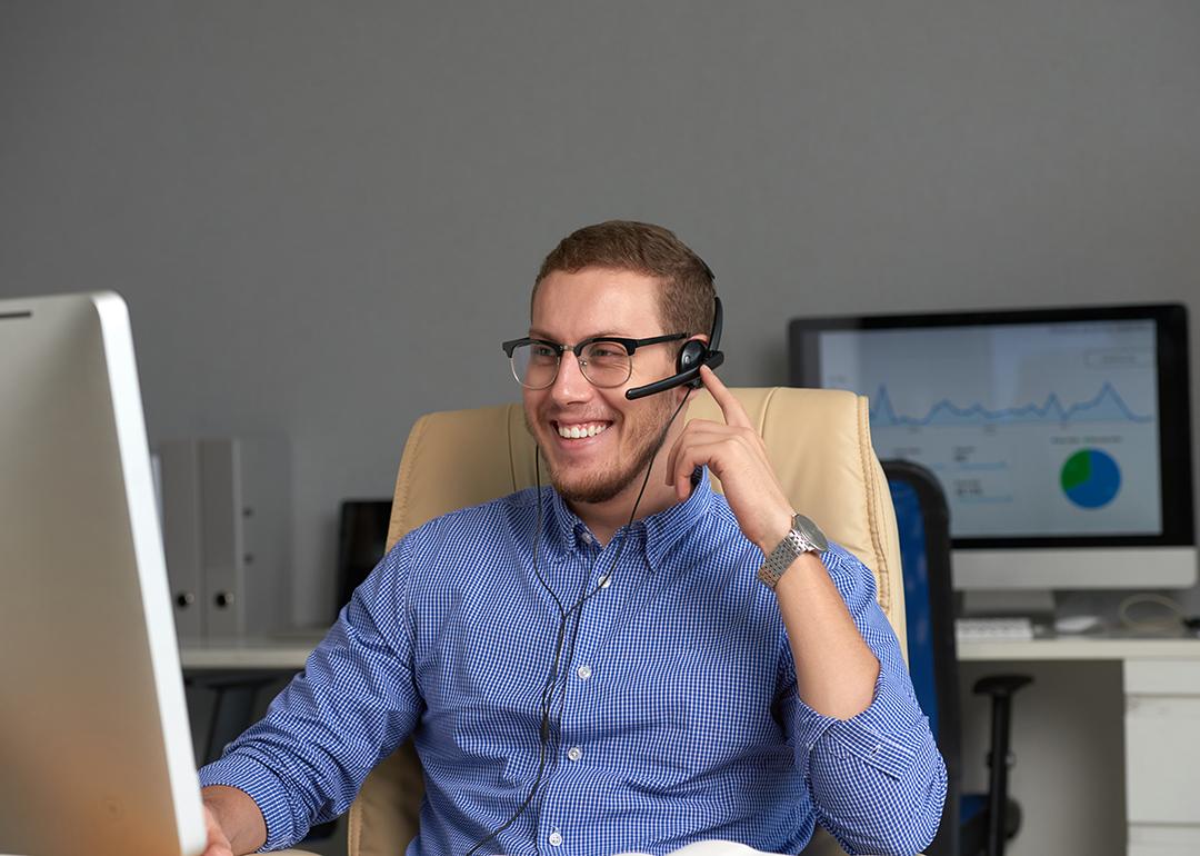 A young businessman in a home office smiling while talking to a client.