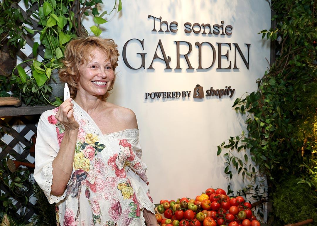 Pamela Anderson poses holding up a lip produce in front of "Sonsie Garden" with Shopify on October 24, 2025 in New York City.