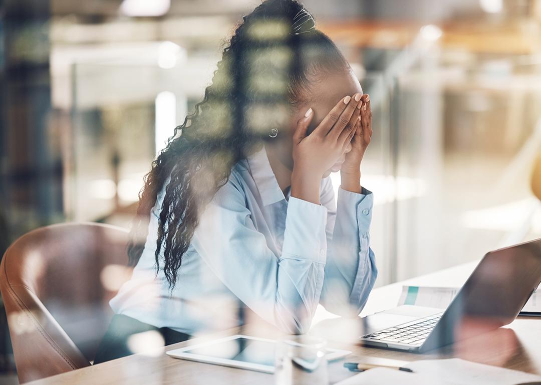 A stressed young black woman with her hands over her face at work.