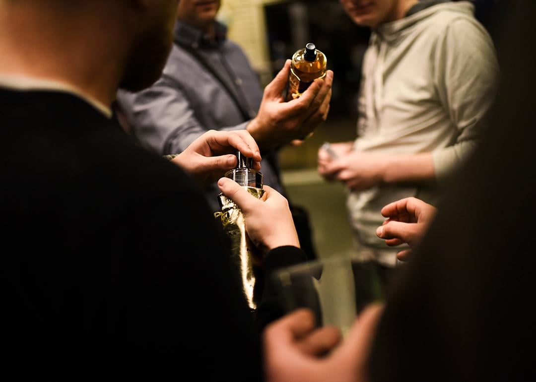 Three men in a room holding perfume bottles and trying out their scents.