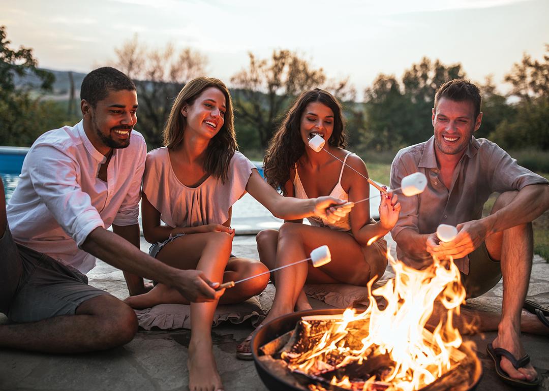 A group of four friends around a campfire grilling s'mores.