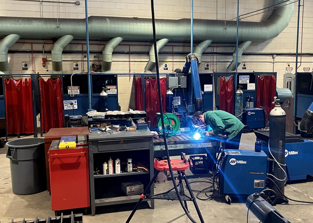 A welding demonstration taking place at a summer program in Philadelphia, colorful stations are in the background. 