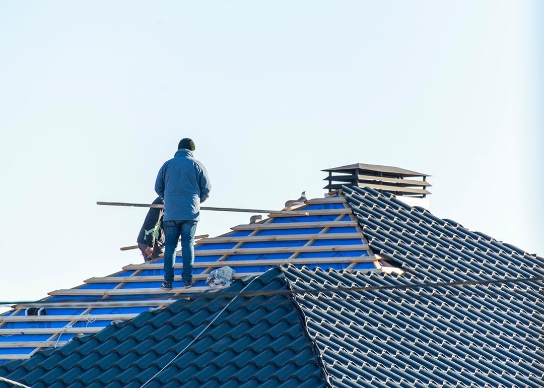 Workers installing metal tile on the roof while roofing house in construction site.