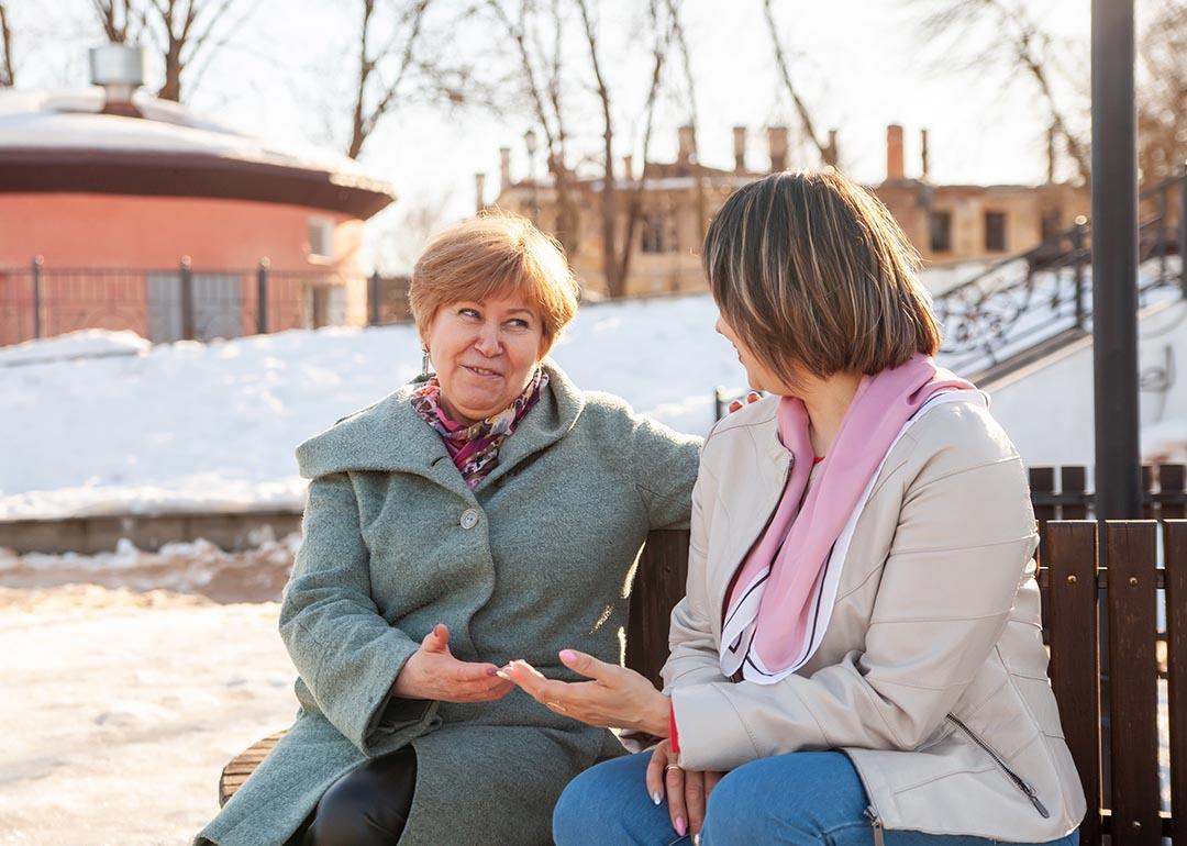 Contemplative casual middle-aged women sitting on bench winter, chatting.