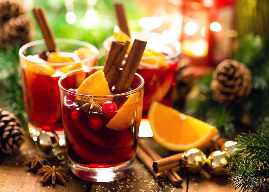 Christmas mulled red wine with spices and oranges on a wooden rustic table with evergreen decor and pine cones in the background.