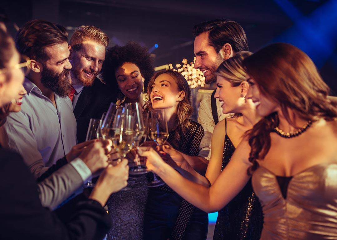 A group of people in party dresses and suits clink glasses together in a party setting.