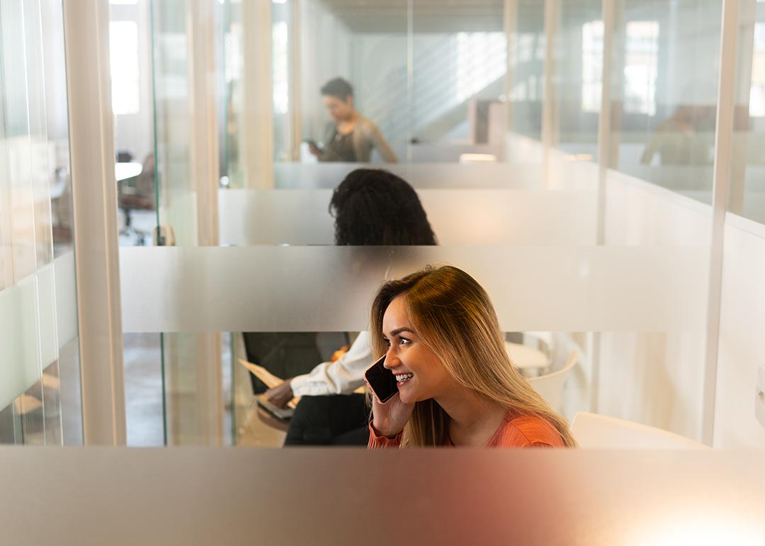 A woman at an office's phone booth taking a call with her smartphone.