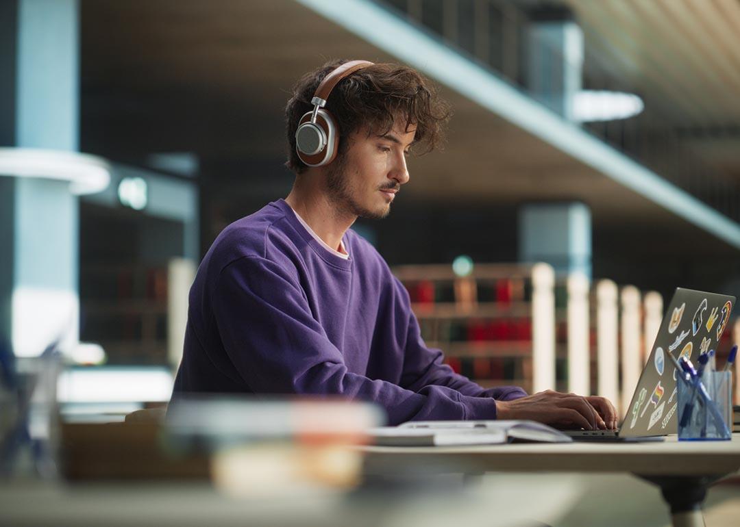 Person wearing purple sweatshirt and phones working on laptop in library. 
