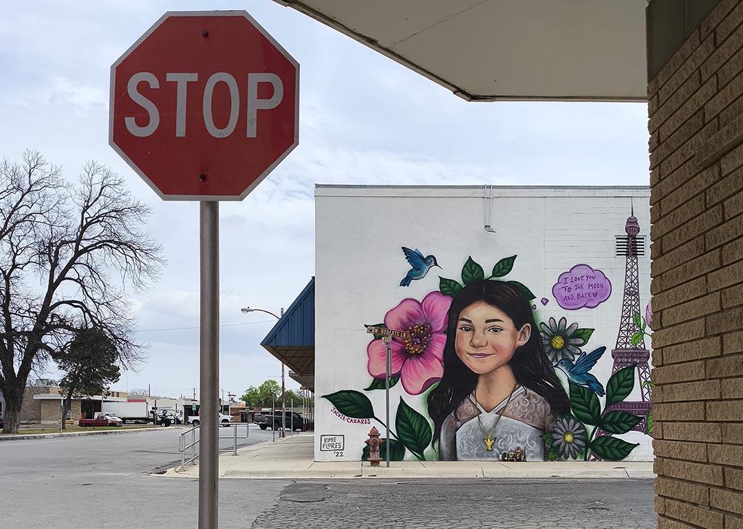 A murals of shooting victims in Uvalde painted on a wall behind a stop sign.