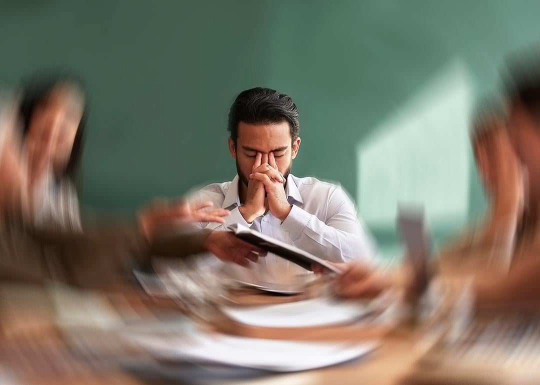 A male employee seated at the center of an office table with his surroundings are illustrated with a motion blur.