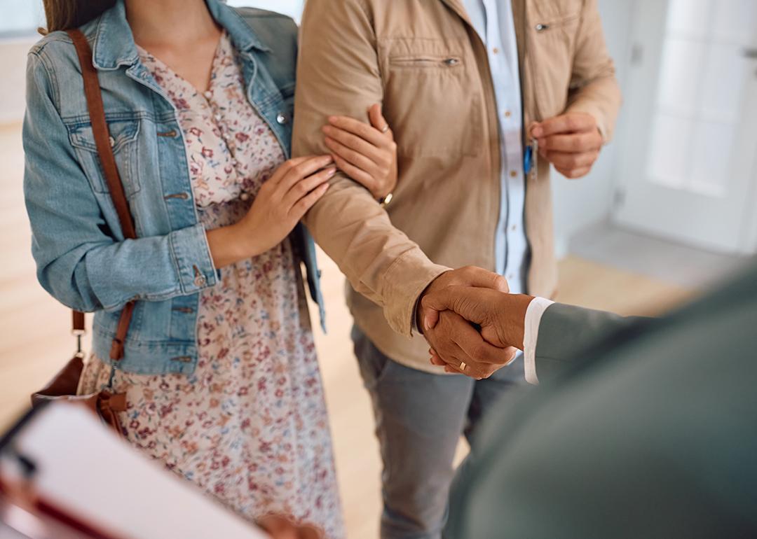 A couple shaking hands with a real estate agent after purchase.
