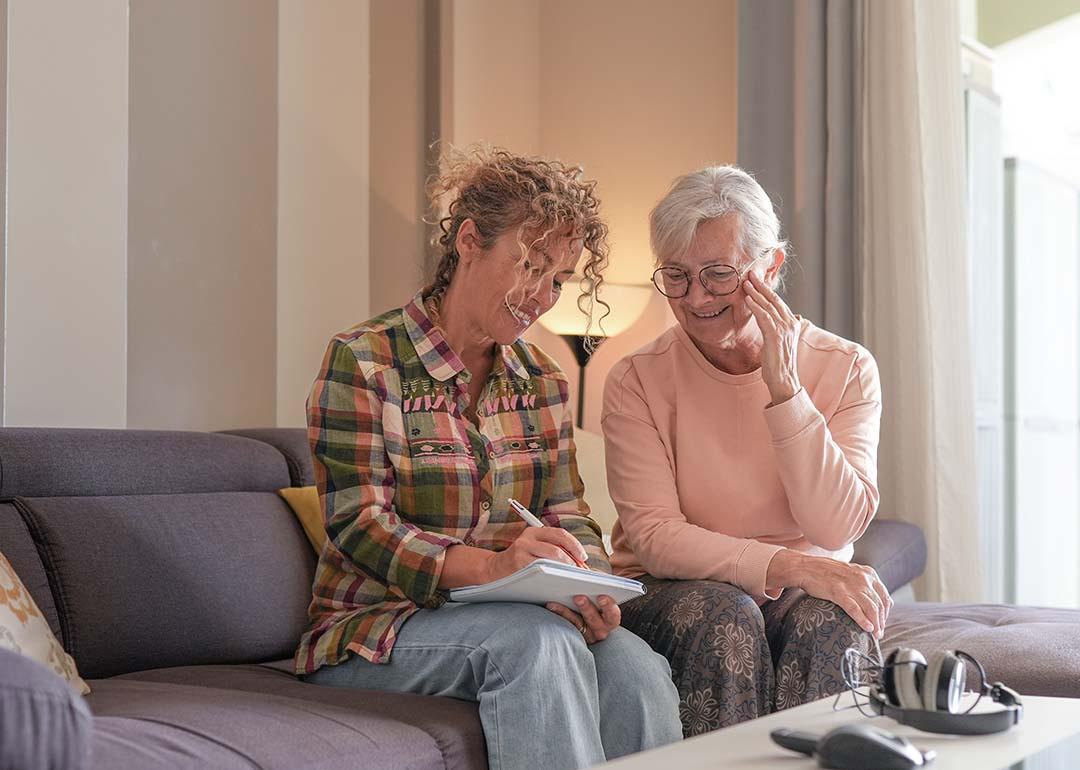 A senior woman and her caregiver sitting together on a sofa at home.