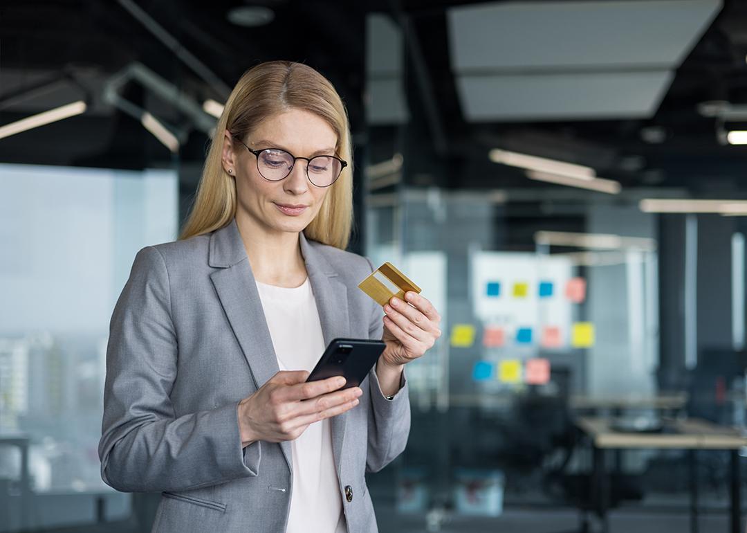 A businesswoman holding a phone and a credit card in an office.