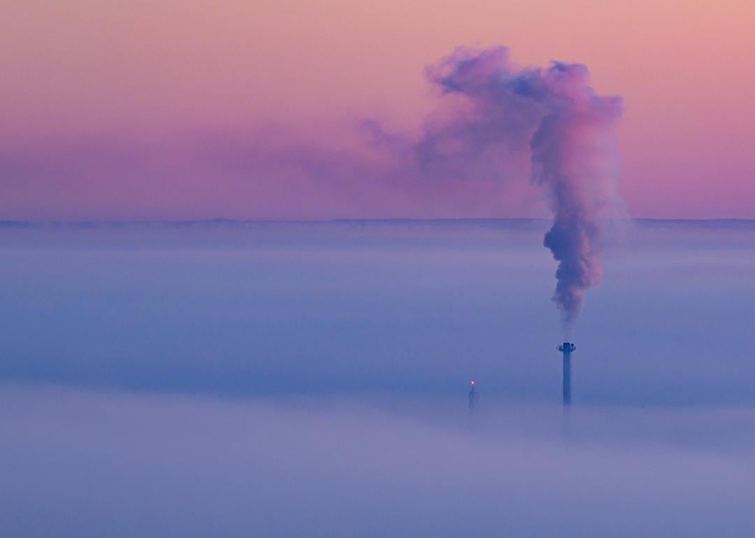 Smoke coming out of a heat and power plant chimney, blending with a lavender morning sky.