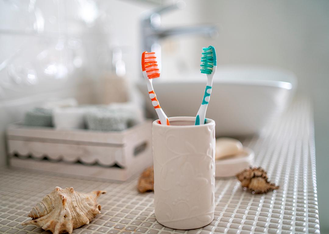 Two colorful toothbrushes in a ceramic glass against the background of a bathroom's washbasin.