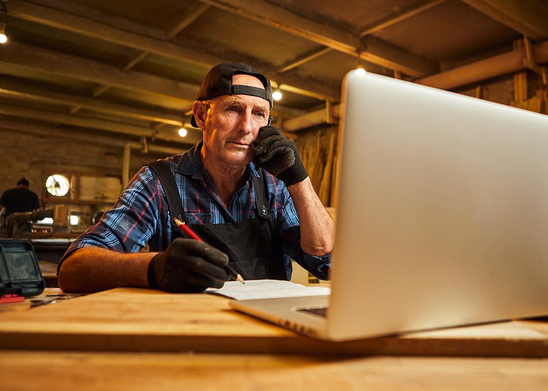 A senior male carpenter working with a client online from their workshop.