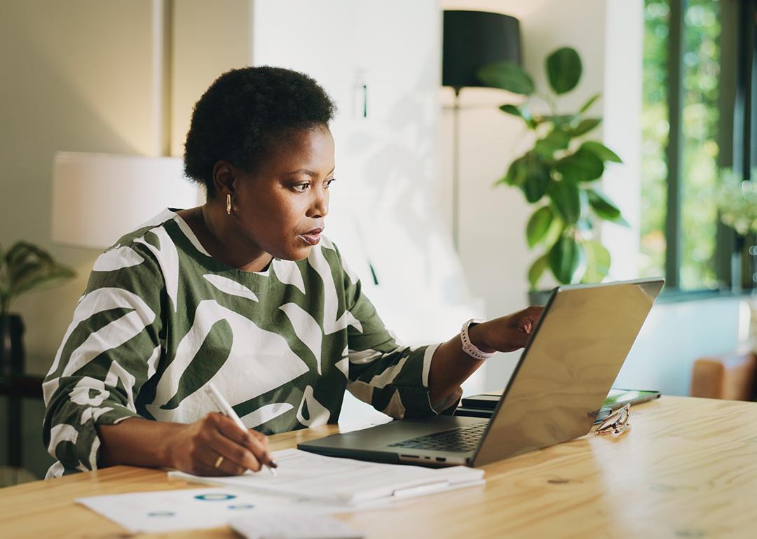 A black female bookkeeper working with a laptop and financial reports at home.