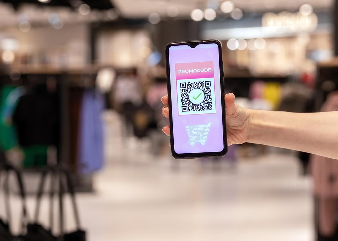 A woman's hand holding a phone displaying promo code applied by scanning a QR code inside a shopping mall.