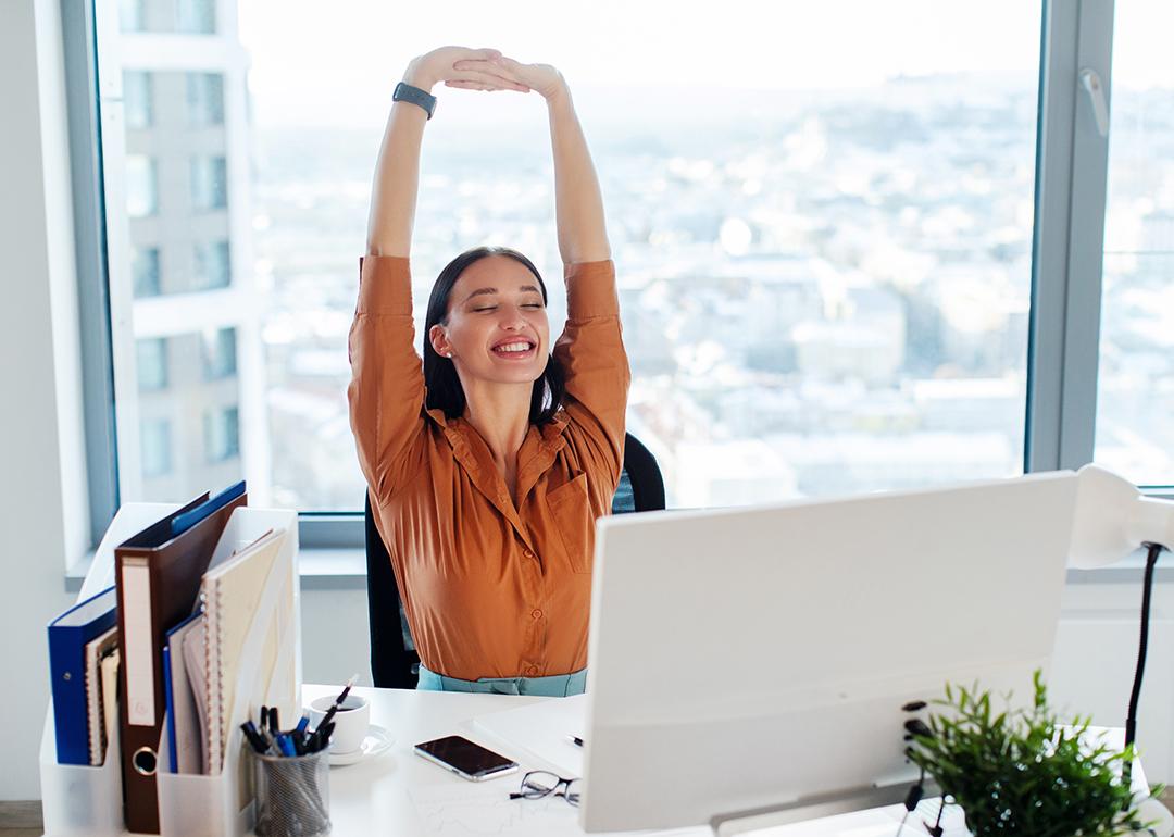 A female manager happily stretching her back and arms while seated at her desk in an office.
