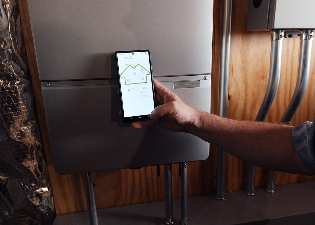 A homeowner using a phone monitoring a battery from Sunrun, a company which provides home solar and batteries. A new partnership between Sunrun, Ford and the Baltimore Gas and Electric Company has resulted in a residential vehicle to grid pilot project.