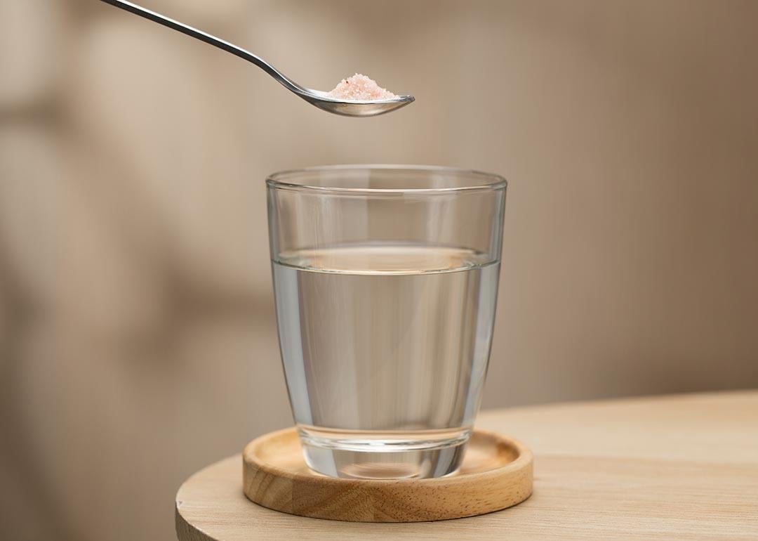 A spoon of Himalayan salt held above a glass of drinking water, highlighting its potential health benefits.