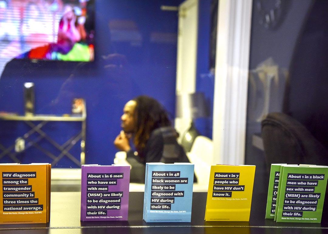 Jon'Aric Nathaniel waits from his clinical appointment at Open Arms Healthcare Center behind a window lined by pamphlets in the foreground on HIV.