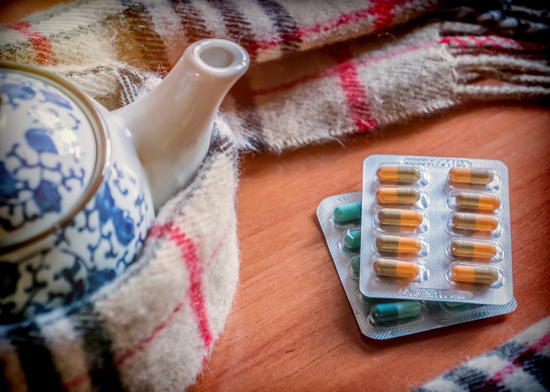 Sheets of pills beside a teapot wrapped in scarf.