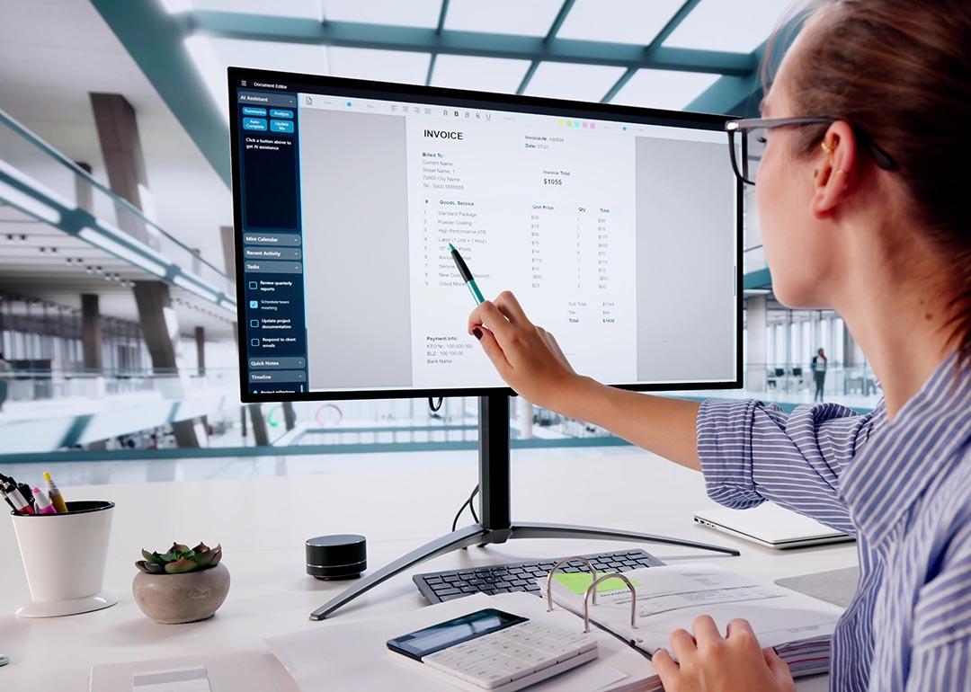 Person pointing out line item on invoice on large computer monitor.