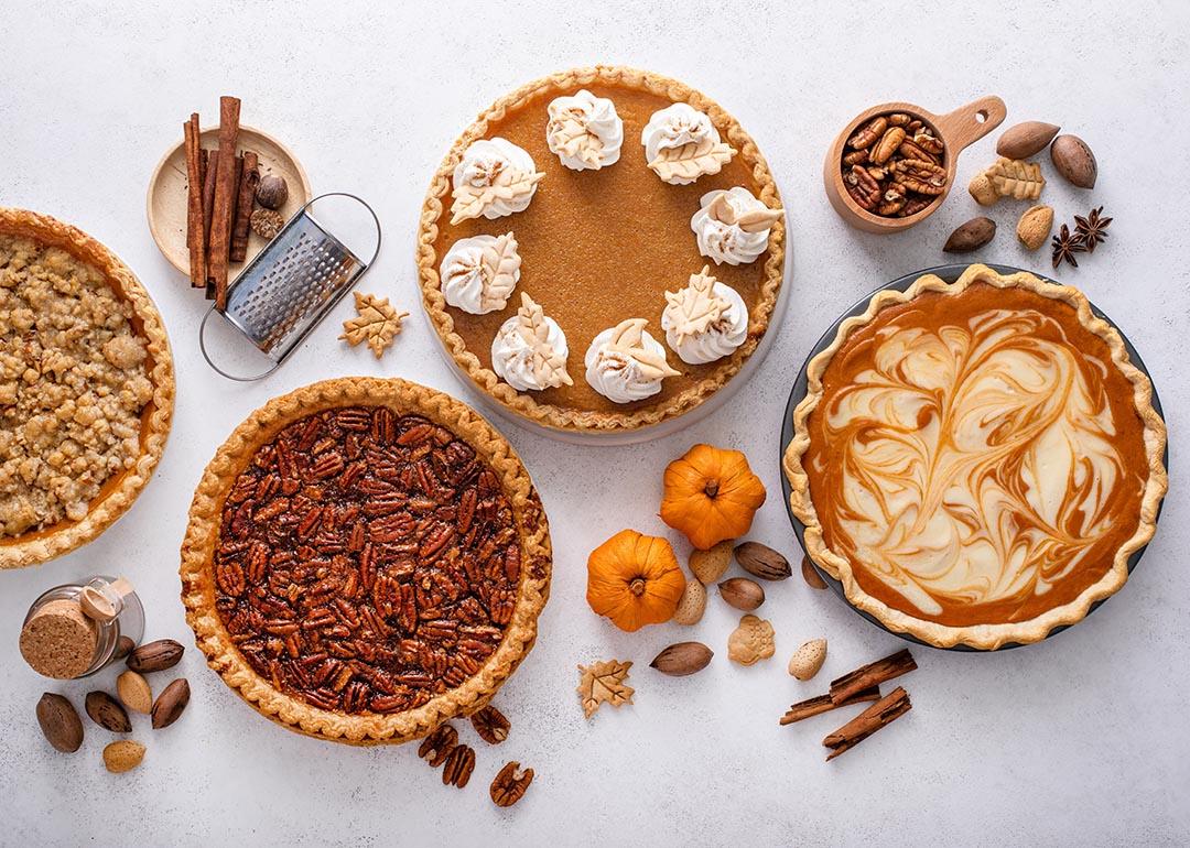 Top-down view of variety of Thanksgiving pies including pumpkin, pecan and cheesecake pumpkin pie on light background.