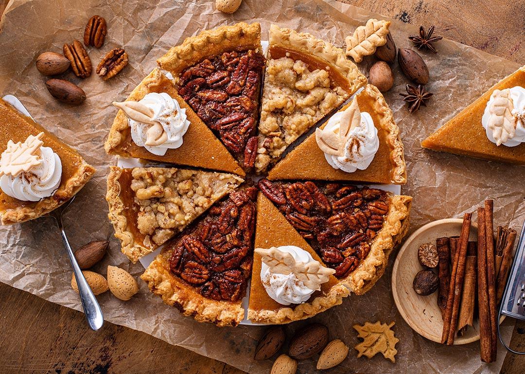 A pie composed of alternating slices of pumpkin with whipped cream and pecan pie, on parchment paper. 