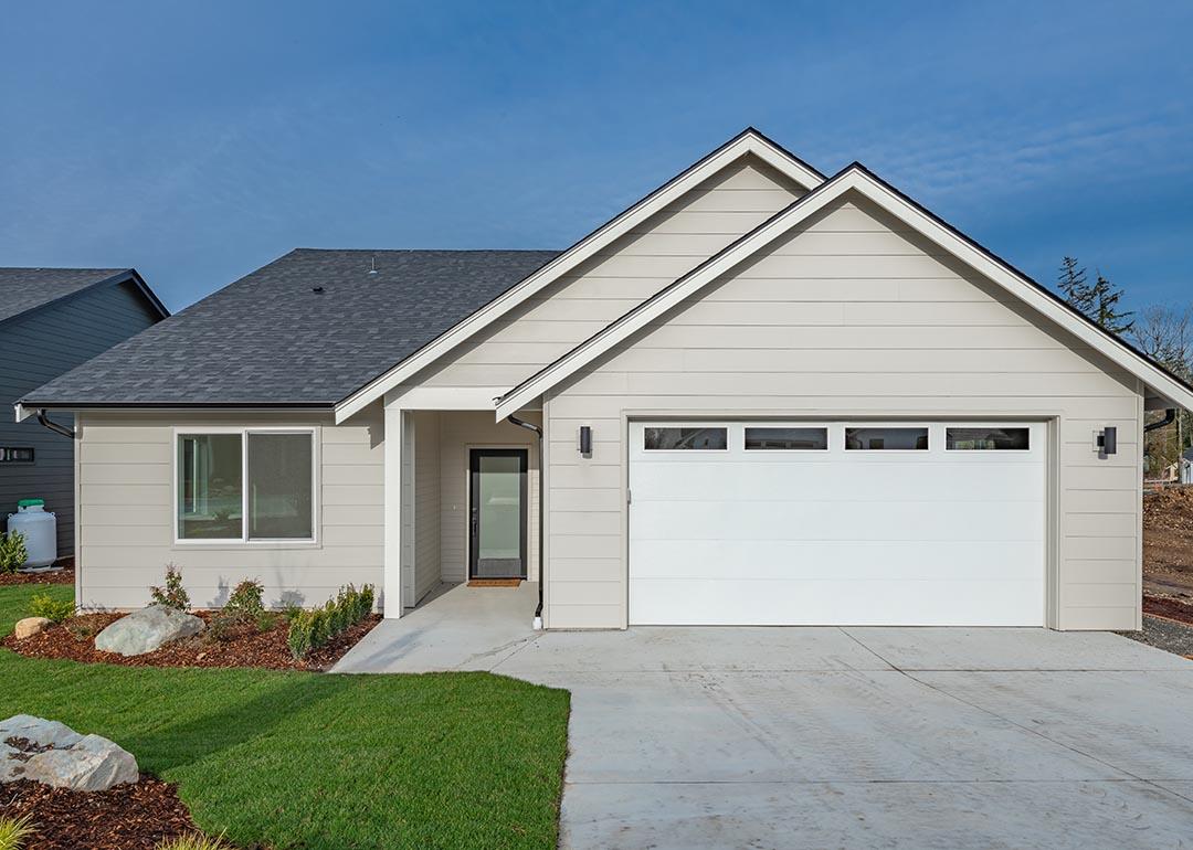 Middle class home exterior small rambler style house with simple style brand new construction blue sky green grass winter season family residence in a suburban neighborhood.