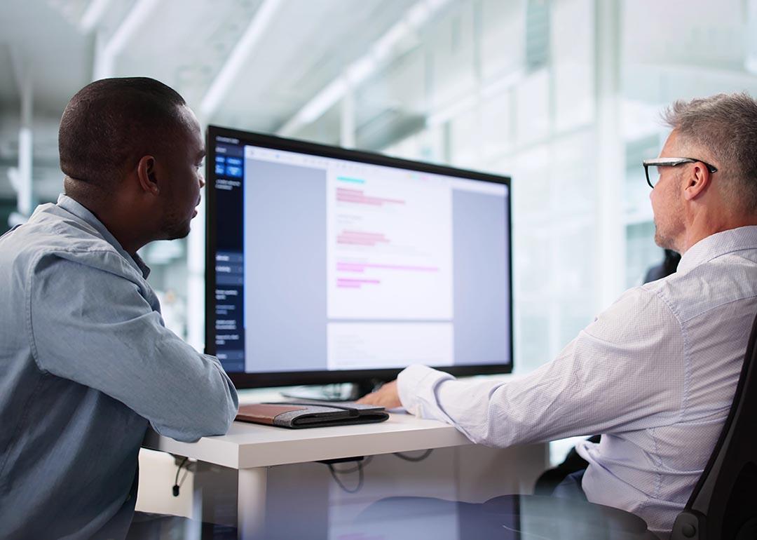 Two people sitting at a desk looking at a large screen; one is a privacy compliance specialist ensuring HIPAA regulations are being followed correctly.