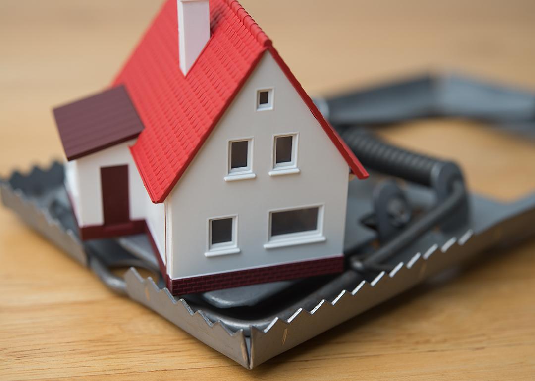 Mortgage scam concept depicted by a figure of a house inside a steel trap.