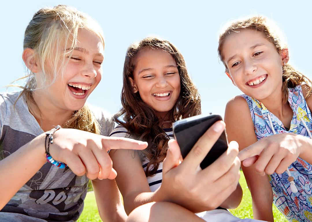 A group of three young girls laughing at content on social media.