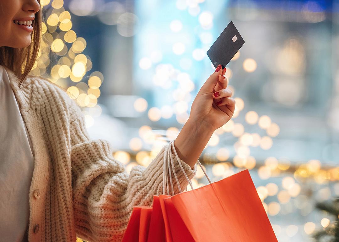 A woman with shopping bags on her arm and holding up a credit card.