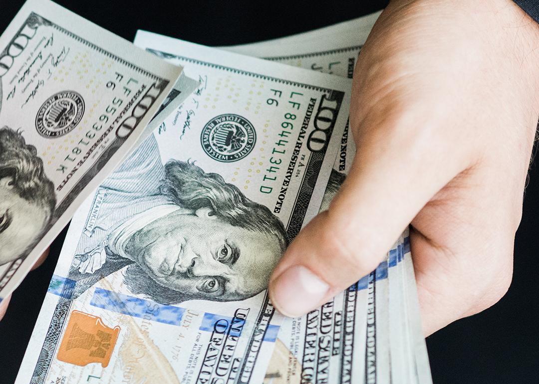 A person's hand counting $100 dollar bills.