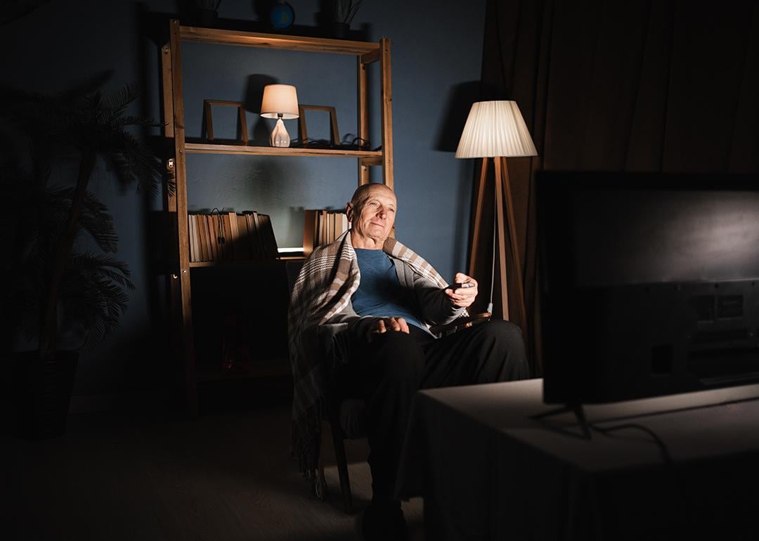 An elderly man sitting in a dim living room and watching TV.