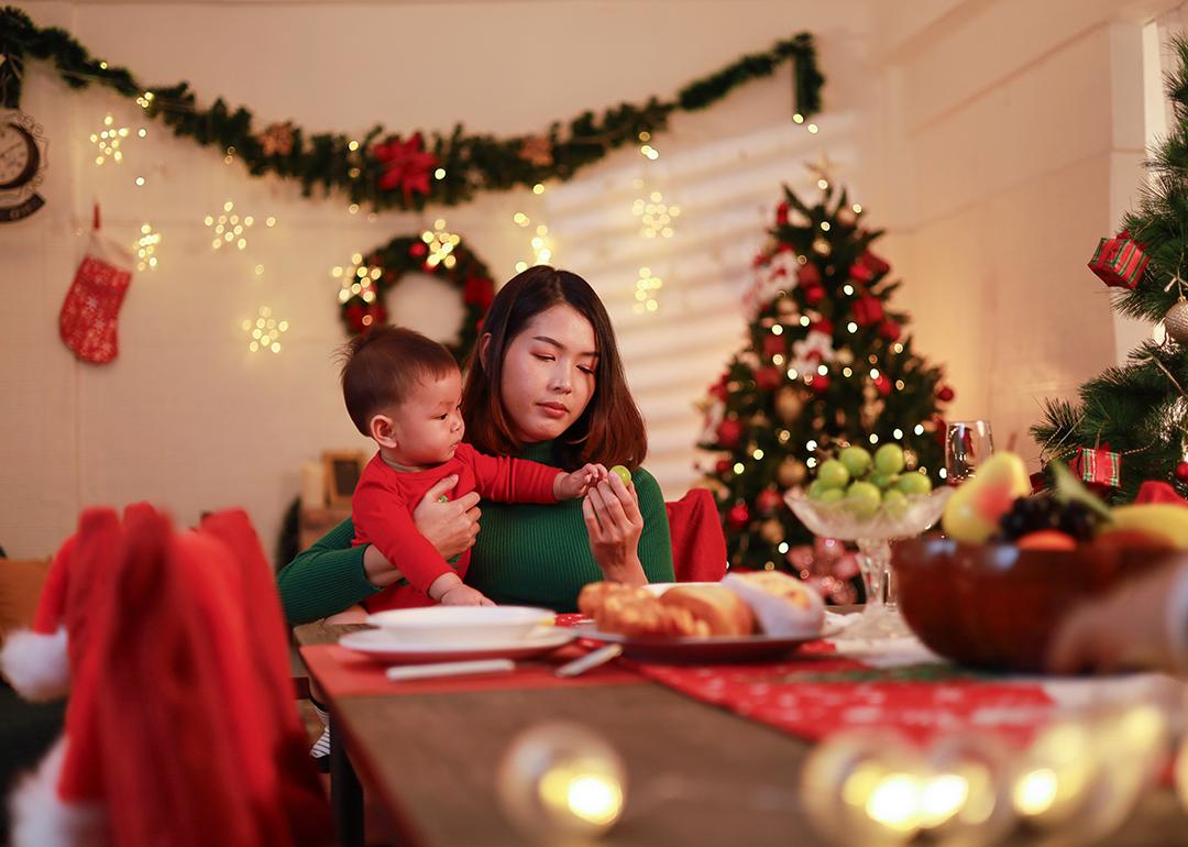 A young mother sitting alone with holding her baby at the dinner table during Christmas Eve.