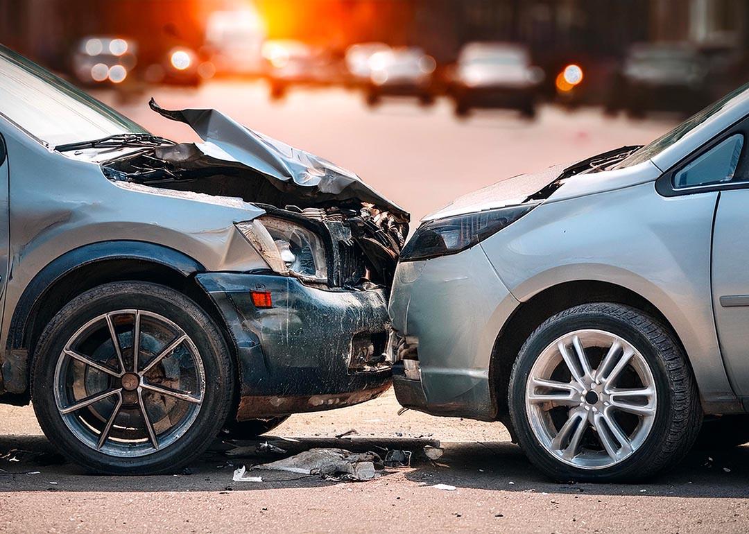 Side view of two silver cars that are stopped in a collision with the hood of one car visibly damaged.