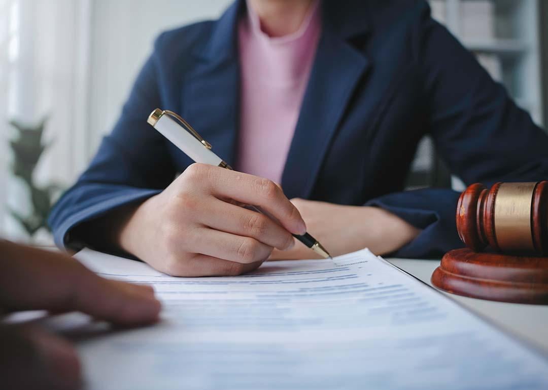 Torso of a female lawyer signing a document for a client in their office.