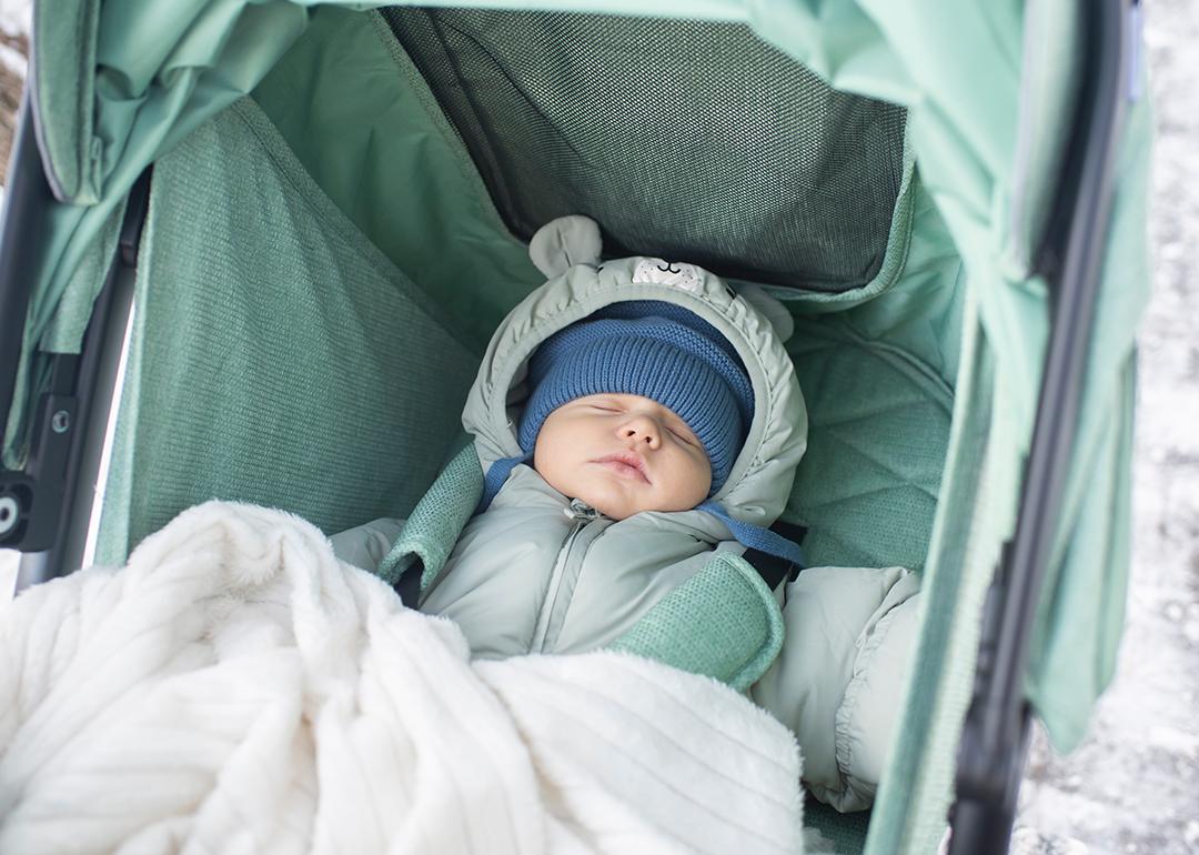 A baby in winter clothes sleeping in a green stroller outdoors.