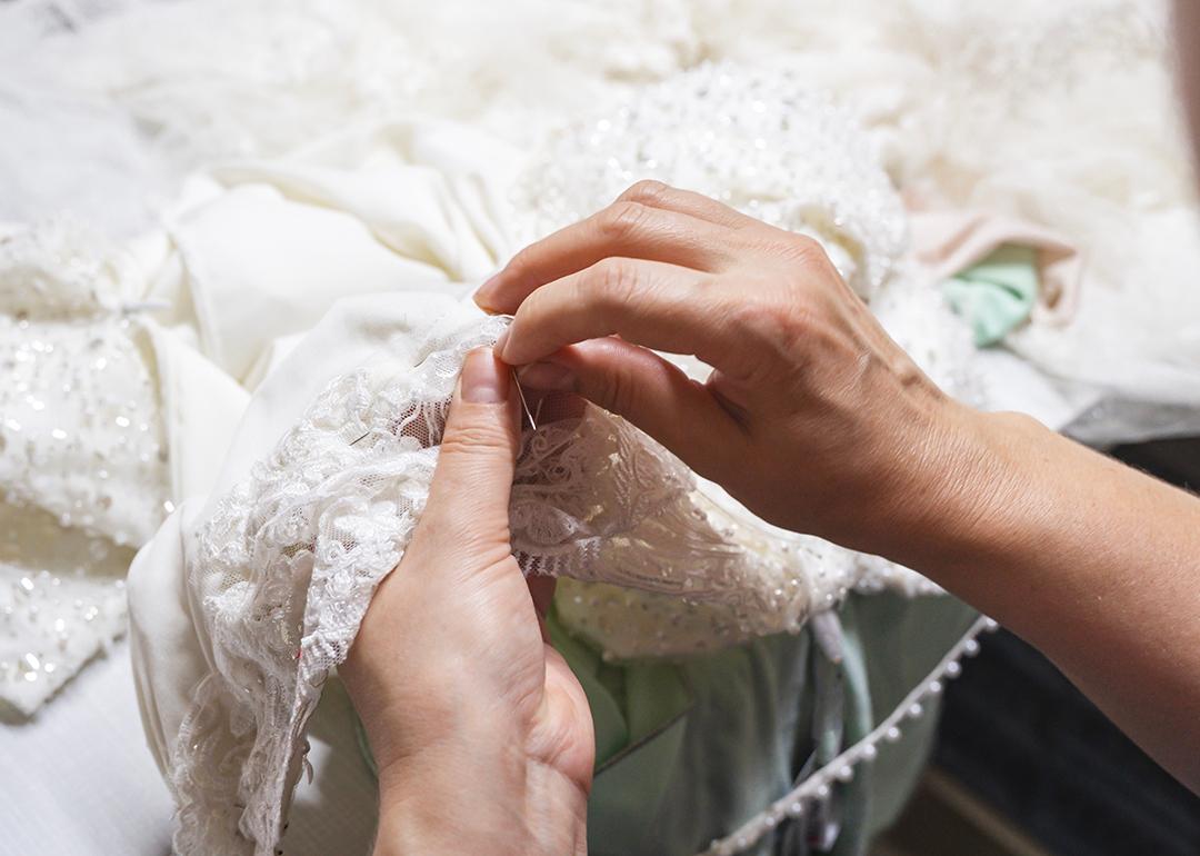 Hands of a seamstress sewing beads on a wedding dress.