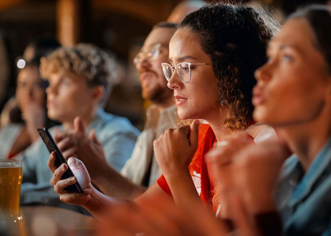 A female football fan in a bar monitoring game results on her phone.