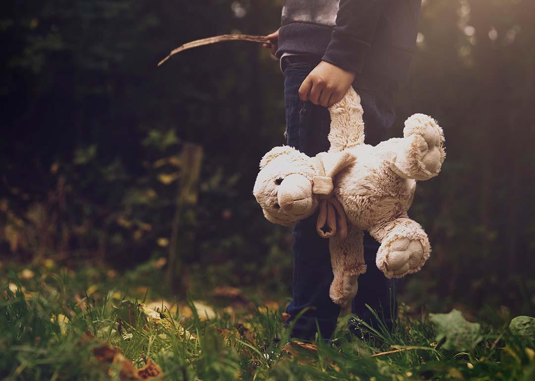A young boy holding a teddy bear outdoors.