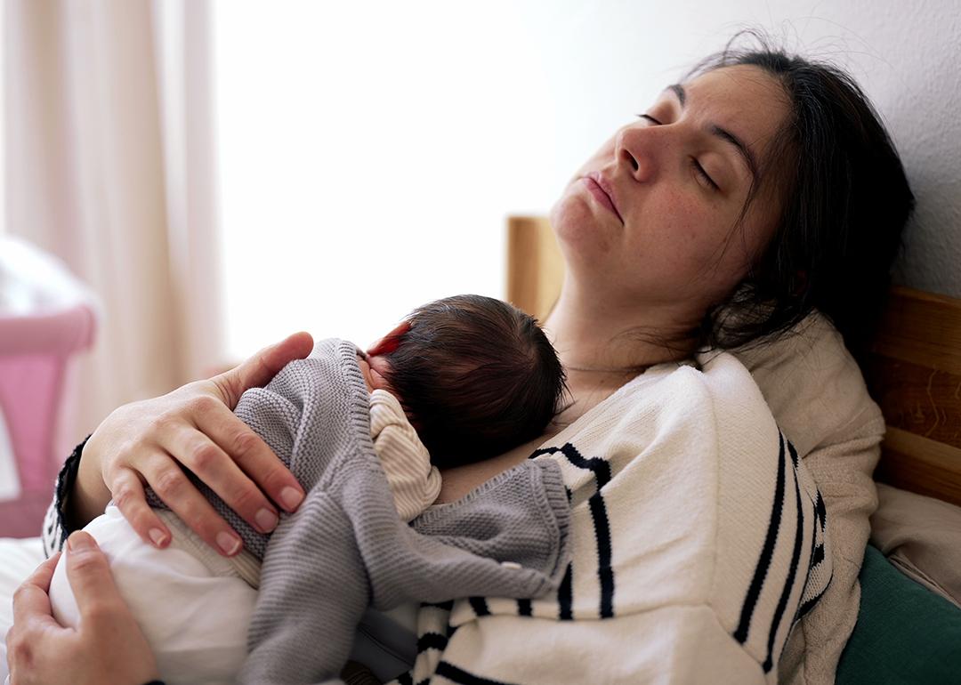 A tired mother sleeping with her newborn on her chest.