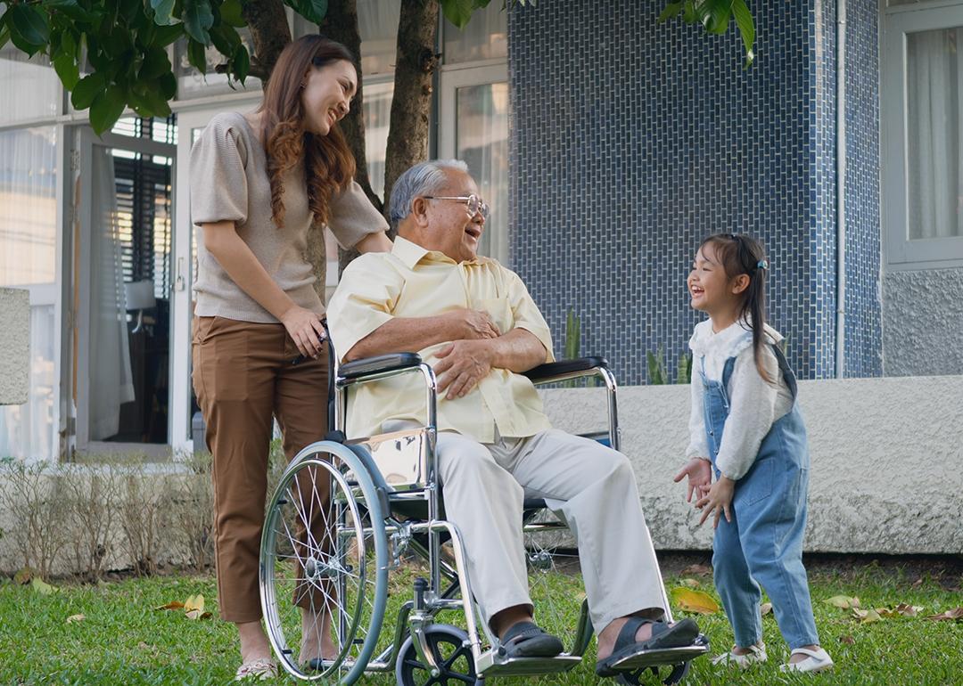 A disabled senior grandfather with his daughter and grandchild in a park.